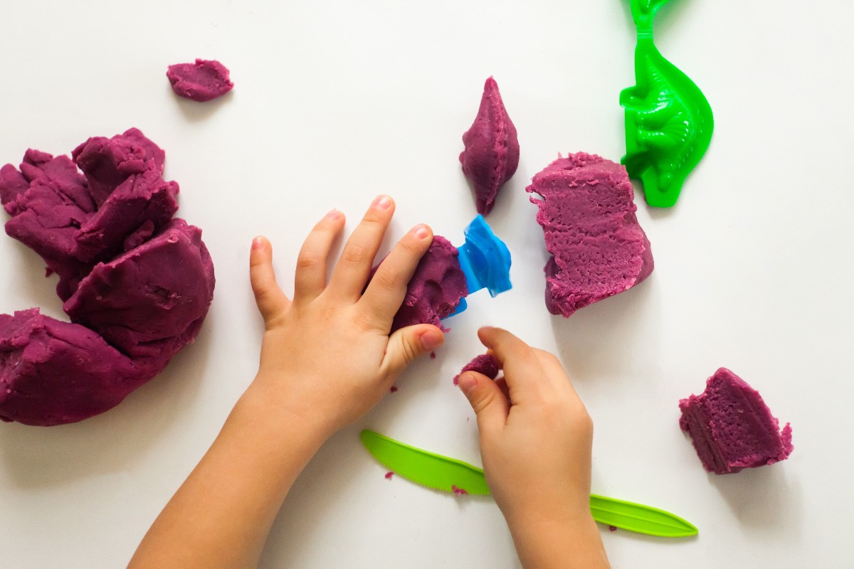 Child's hands playing with purple clay and plastic dinosaur toys