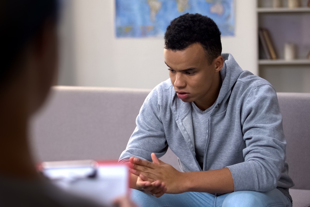 teen boy in a gray hoodie sitting on a sofa looking serious