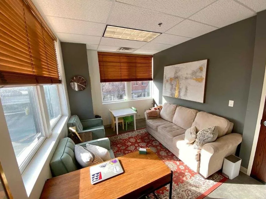 Therapy office with sage green walls and a sofa with light coming in through the windows