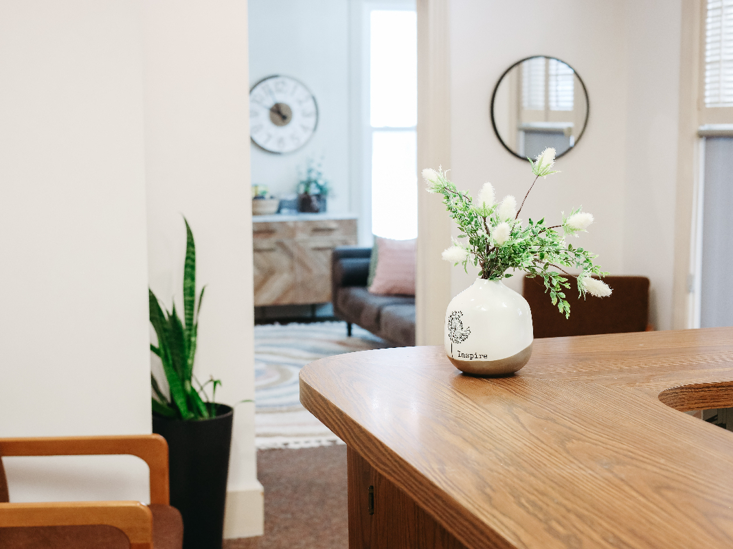 Office with cream colored walls and a white vase of white flowers sitting on a wooden desk.